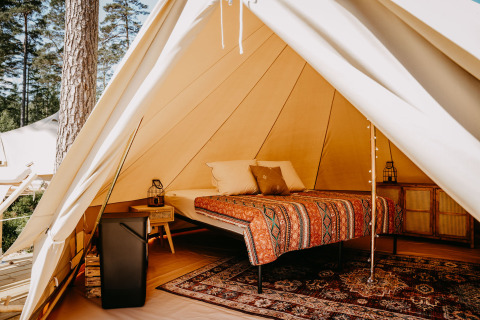 Sfeervol interieur van een luxe glampingtent met comfortabel bed, vloerkleed en meubels in het bos.