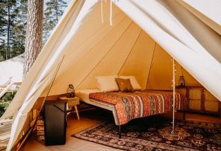 Sfeervol interieur van een luxe glampingtent met comfortabel bed, vloerkleed en meubels in het bos.