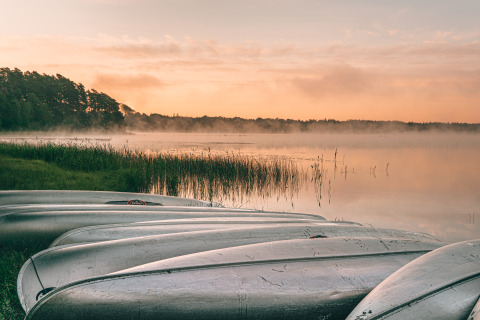 Boten aan de oever van een rustig meer bij zonsopgang, Nordic Woods - Wildernis Glamping Zweden, Zweden.