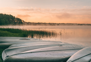 Boten aan de oever van een rustig meer bij zonsopgang, Nordic Woods - Wildernis Glamping Zweden, Zweden.