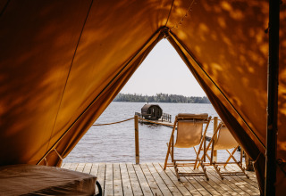 Uitzicht vanuit tent op meer, twee stoelen op houten terras en sauna op steiger, Nordic Woods Wildernis Glamping Zweden