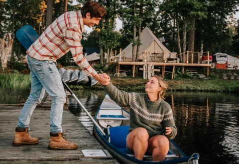Koppel glamping bij Nordic Woods - Wildernis Glamping Zweden, vrouw in kano terwijl man haar op steiger helpt.