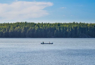Twee mensen kanoën op een rustig meer met bos op de achtergrond bij Nordic Woods - Wildernis Glamping Zweden.