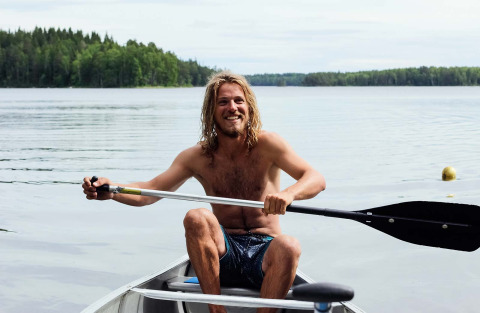 Jonge man peddelt in een kano op een rustig meer bij Nordic Woods - Wildernis Glamping Zweden.