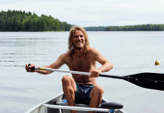 Jonge man peddelt in een kano op een rustig meer bij Nordic Woods - Wildernis Glamping Zweden.