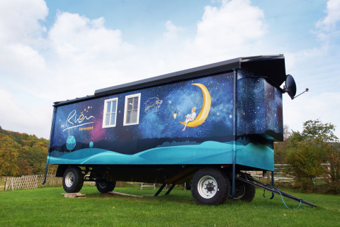 Alojamiento glamping en Turingia, carro gitano decorado con cielo estrellado y luna sobre césped verde.