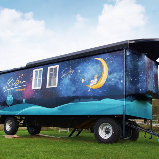 Glamping-Unterkunft in Thüringen, bemalter Zirkuswagen mit Sternenhimmel und Mondmotiv auf grüner Wiese.