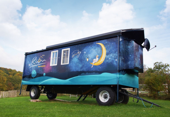 Glamping accommodatie in Thüringen, beschilderde zigeunerwagen met nachtelijke hemel en maan op grasveld.