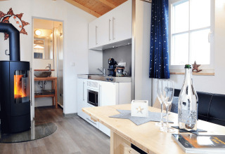 Moderne Glamping-Unterkunft mit Holzboden, Kamin, Küchenzeile, Esstisch und hellen Fenstern.