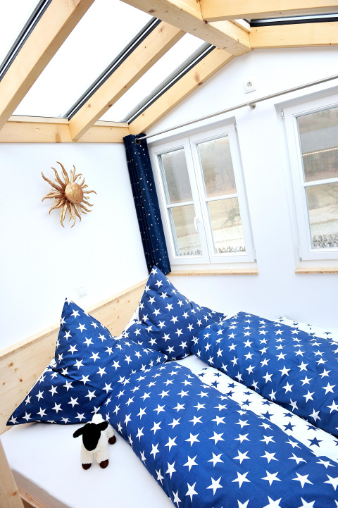 Interno di una sistemazione glamping con biancheria blu a stelle, lucernario e finestre ampie in Turingia.