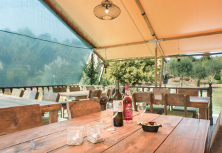 Überdachter Essbereich bei Quinta do Cascalhal - Safaritenten Braga mit Holzbank, Weinflaschen und Gläsern.