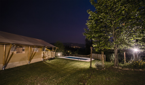 Site de glamping éclairé avec tentes safari, piscine et arbres la nuit à Quinta do Cascalhal, Braga, Portugal.