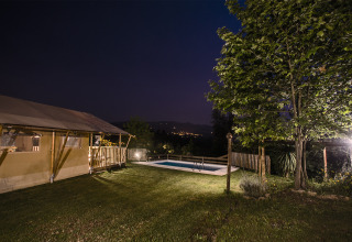 Site de glamping éclairé avec tentes safari, piscine et arbres la nuit à Quinta do Cascalhal, Braga, Portugal.