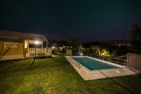 Night view of Quinta do Cascalhal - Safaritenten Braga showing illuminated glamping tent and pool in nature.