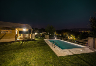 Nachtaufnahme von Quinta do Cascalhal - Safaritenten Braga mit beleuchtetem Zelt und Pool in Naturumgebung.