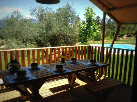 Terrasse mit Holztisch, gedeckt für vier, Pool und grüner Naturblick bei Quinta do Cascalhal - Safaritenten Braga.