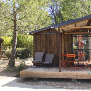 Hébergement glamping Huttopia Fontvieille en Provence, cabanes en bois sous les arbres avec terrasse ensoleillée.