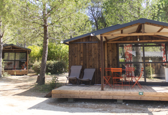 Glamping-Unterkunft bei Huttopia Fontvieille in der Provence mit Holzchalets zwischen Bäumen und Terrassen.