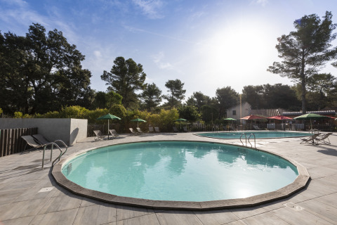 Outdoor swimming pool area with lounge chairs and umbrellas at Huttopia Fontvieille – Glamping Provence.