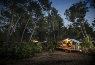 Glamping bei Huttopia Fontvieille – Provence, beleuchtetes Safarizelt im bewaldeten Campingplatz am Abend.