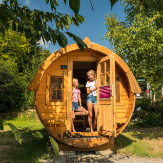 Zwei Personen genießen Glamping in einem Weinfass auf Camping im Bergischen Land, umgeben von Bäumen.