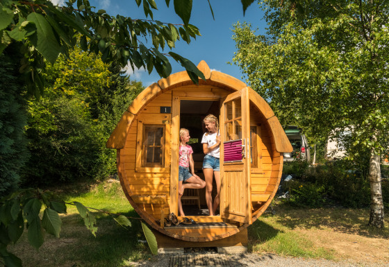 Deux personnes profitent du glamping dans un tonneau au Camping im Bergischen Land, entourées de verdure.