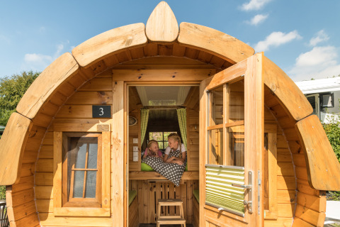 Two children relax inside a wooden cabin at Camping im Bergischen Land glamping under a sunny blue sky.
