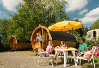 Gezin geniet van een maaltijd buiten bij wijnvat-glampingaccommodatie op Camping im Bergischen Land in de zon.