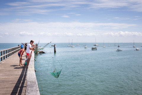 Familias pescando desde un muelle de madera junto a veleros en Huttopia Noirmoutier - Glamping Vendée.