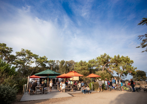 Espace repas en plein air avec parasols colorés et invités au Huttopia Noirmoutier Glamping en Vendée, France.