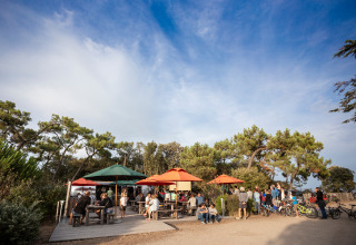 Espace repas en plein air avec parasols colorés et invités au Huttopia Noirmoutier Glamping en Vendée, France.