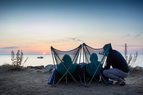 Drei Menschen entspannen am Strand in Campingstühlen und genießen den Sonnenuntergang bei Huttopia Noirmoutier.