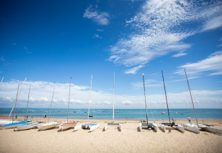 Voiliers alignés sur la plage de sable avec vue sur la mer et le ciel bleu à Huttopia Noirmoutier - Glamping Vendée.