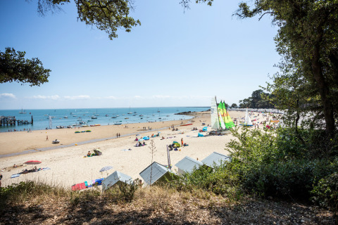 Beach view at Huttopia Noirmoutier - Glamping Vendée with tents, beach huts, and sailboats on the water.