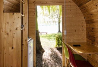 Intérieur d’un pod en bois avec bureau, chaises et porte ouverte sur arbres près du lac de Constance, camping.
