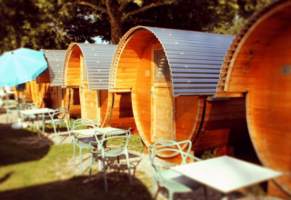 Reihe von Schlaf-Fässern aus Holz mit Sitzgelegenheiten im Freien auf dem Campingplatz Markelfingen am Bodensee.