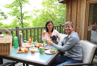 Pareja desayunando con su perro en la terraza de Baumpalast Boomhutten, Baden-Württemberg, rodeados de naturaleza.