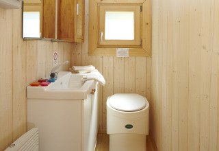 Lyst badeværelse i træ med toilet og håndvask i glamping-indkvartering i Baumpalast Boomhutten, Baden-Württemberg.