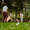 Family playing badminton by tipis in a green forest at Camping de Marcourt, Belgian Luxembourg.