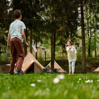 Familie speelt badminton voor tipi’s in het bos bij Camping de Marcourt, Belgisch Luxemburg.
