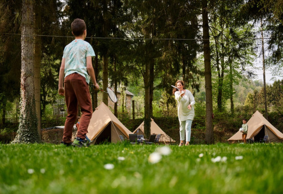 Familia jugando bádminton frente a tipis en el bosque en Camping de Marcourt, Luxemburgo belga.