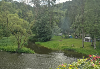 Campingplatz an einem Fluss mit Tipizelten, Wohnwagen und grünen Bäumen bei Camping de Marcourt, Belgisch Luxemburg.