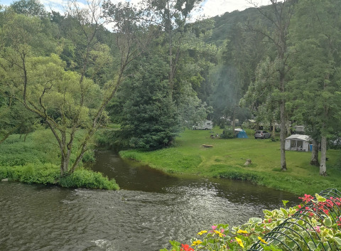 Camping aan een rivier met tipitenten, caravans en groene bomen bij Camping de Marcourt in Belgisch Luxemburg.