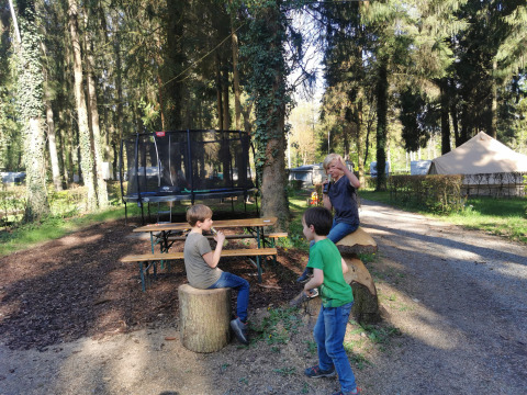 Kinder spielen an einem Picknicktisch und Baumstümpfen bei einem Waldcampingplatz mit Tipizelt.