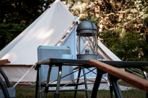 Glamping-Unterkunft mit Zelt, Outdoor-Tisch, Stühlen und Lampe auf dem Camping de Marcourt in Belgisch Luxemburg.