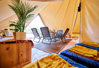 Glamping tent at Camping de Marcourt in Belgian Luxembourg, featuring cozy chairs, plants, and sleeping bags.