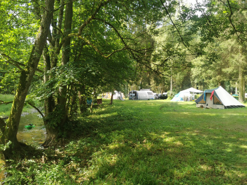 Camping at Camping de Marcourt, Belgian Luxembourg, with tipi tents, green grass and forest near a small stream.