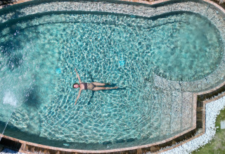 Femme flottant dans la piscine du Procida Camp & Resort - Luxe airstreams glamping, ambiance ensoleillée.