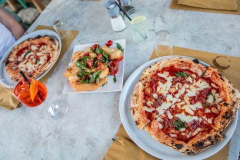 To napolitanske pizzaer og et fad med appetitvækkere på et bord hos PROCIDA Camp & Resort - Luxe airstreams.