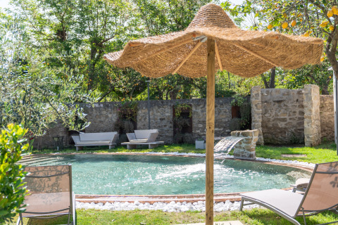 Tuinzwembad met waterval, ligstoelen en rieten parasol bij PROCIDA Camp & Resort - Luxe airstreams glamping.